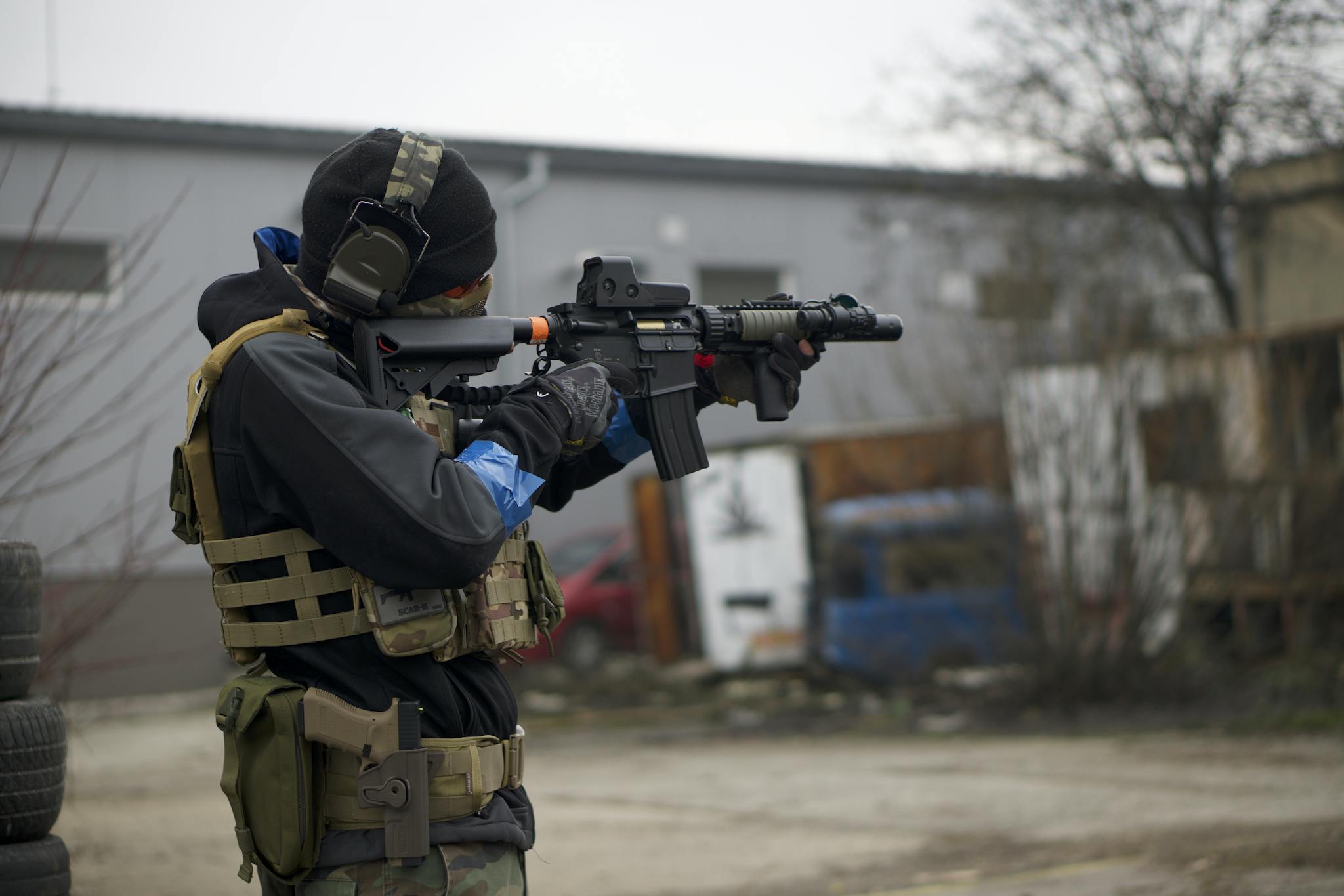 An airsoft player in full tactical gear aiming a rifle outdoors, showing action and focus.